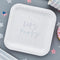 White paper plate with 'Let's Party' text on a gray surface with star decorations.