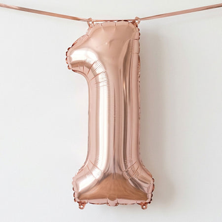 A metallic rose gold foil balloon shaped like the number '1', hanging from a matching rose gold ribbon against a plain white background.