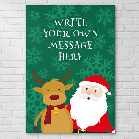 A vertical Christmas-themed poster or print displayed against a white brick wall. The print has a dark green background with lighter green snowflakes, white placeholder text reading 'WRITE YOUR OWN MESSAGE HERE,' a cartoon reindeer with a red scarf, and a cartoon Santa Claus in red and white.