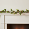 Artificial holly and berry garland draped along a white mantelpiece