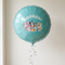 Balloon floating with silver curling ribbon against a neutral wall, in square format