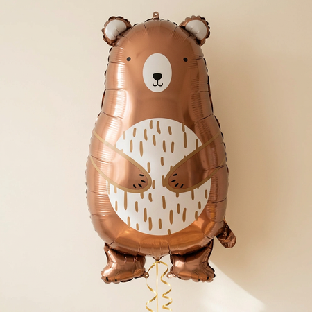 Bear balloon floating with gold curling ribbon against a cream wall with soft light and shade, in square format