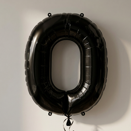 Black number 0 balloon against a softly lit neutral background, in square format