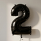 Black number 2 balloon styled to match the number 1, with black curling ribbon and soft light and shade against a neutral wall