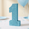 Blue glitter number 1 decoration on a white tablecloth with soft pale blue first-birthday styling