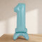 Blue number 1 standing balloon on a wooden tabletop with a cream background and soft light and shade, matching the pink balloon’s styling