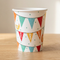 Bunting-print paper cup on a wood table with a neutral background and soft light and shade, square format