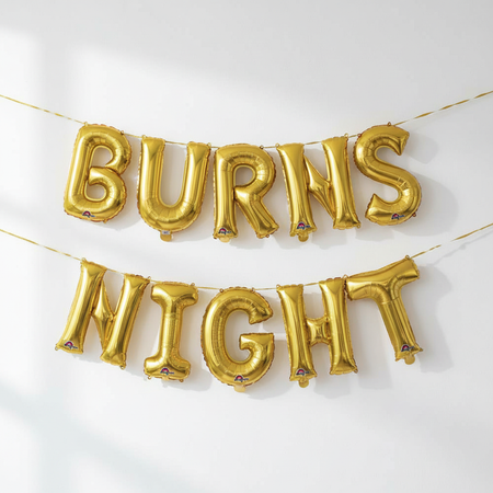 BURNS NIGHT letter balloons hung on a continuous gold ribbon through each letter