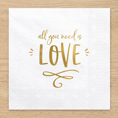 Close-up All You Need Is Love napkin on a wood surface, retaining the overhead perspective and square format
