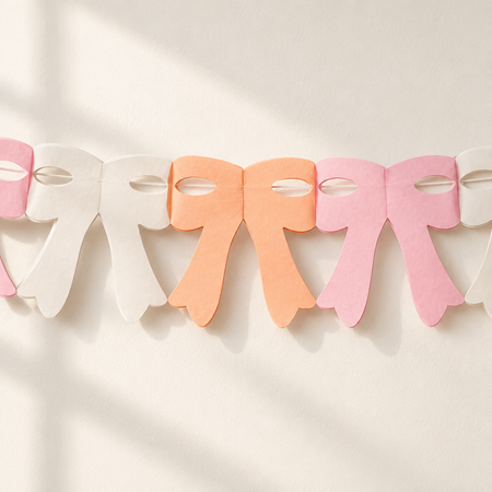 Close-up of peach, pink and ivory paper bow bunting against an off-white wall