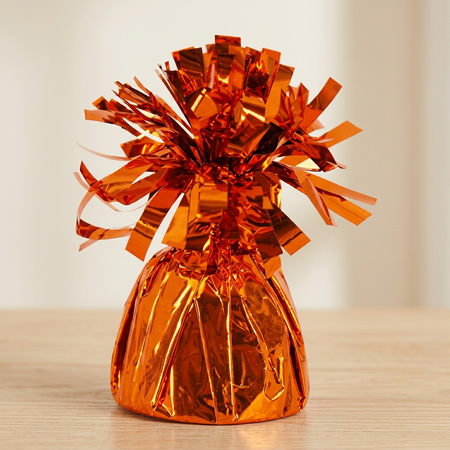 Close-up of the orange foil balloon weight on a matching wooden table with a neutral background, in square format