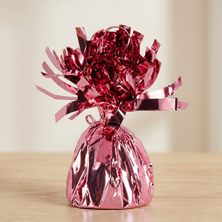 Close-up of the pink foil balloon weight on a matching wooden table with a neutral background, in square format