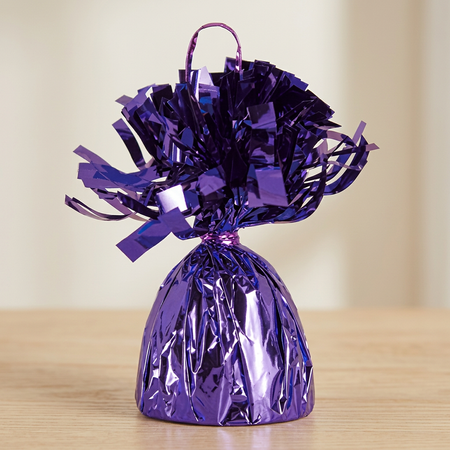 Close-up of the purple foil balloon weight on a wooden table with a neutral background, in square format