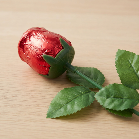 Close-up of the upper half of a foil-wrapped chocolate rose lying on a wooden table