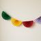 Close-up paper fan bunting against a cream wall with soft light and shade, showing fewer pennants in square format