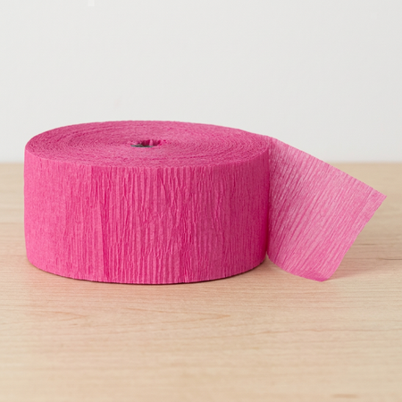 Close-up pink crepe paper streamer roll on a wooden table with a neutral background