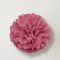 Close-up pink tissue pom pom hanging against a white wall with soft light and shade