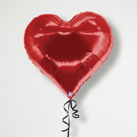 Close-up red heart foil balloon with black curling ribbon emerging from behind the bottom, against a white wall with light and shade