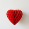 Close-up red honeycomb heart hanging against a white wall with soft light and shade