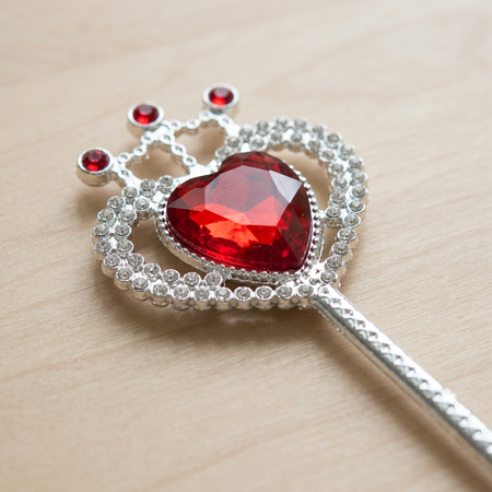 Close-up silver wand with a red heart jewel on a wooden table