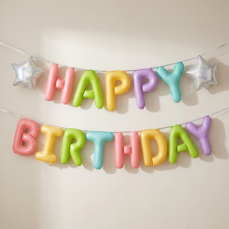 Colourful Happy Birthday balloon letters strung with silver ribbon against a neutral wall, in square format