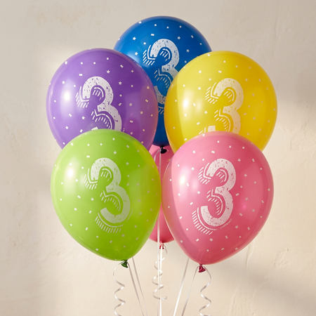 Five assorted number 3 birthday balloons floating with white curling ribbon against a neutral background, close up in square format