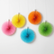 Five colourful paper fans on a plain white wall with natural light and gentle shadows, in square format