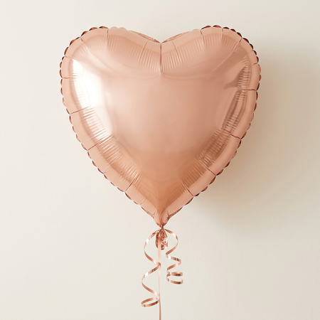 Floating rose-gold heart balloon with matching curling ribbon against a neutral wall with soft light and shade, in square format