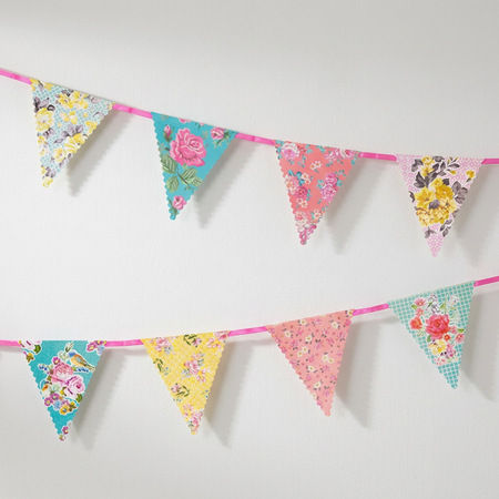 Floral paper bunting against a white wall with soft light and shade, in square format