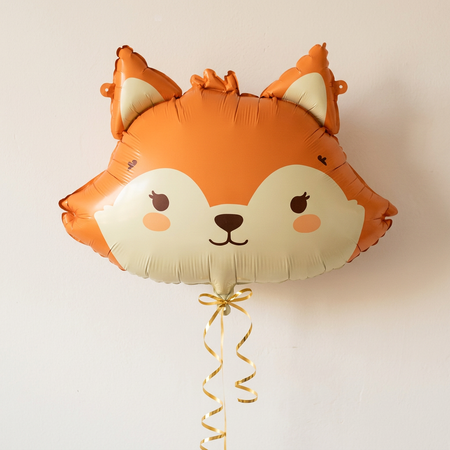 Fox balloon floating with gold curling ribbon against a neutral wall, in square format