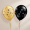 Two decorative balloons, one metallic gold and one black, both printed with white and black starburst and swirl patterns, tied with spiral ribbons against a neutral beige background.