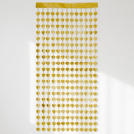 Gold heart foil curtain hanging against a white wall with soft light and shade