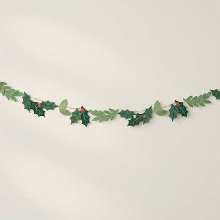Holly and berry paper garland strung across an off-white wall