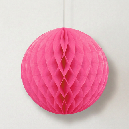 Hot pink honeycomb ball hanging against the matching white wall with soft light and shade
