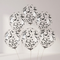Six clear latex balloons filled with black circular confetti against a plain pale-grey background