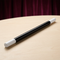 Single black magic wand with white tips on a pale tabletop with a burgundy curtain background