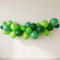 Green mix balloon arch with lime, emerald and dark green balloons mounted against a plain off-white wall