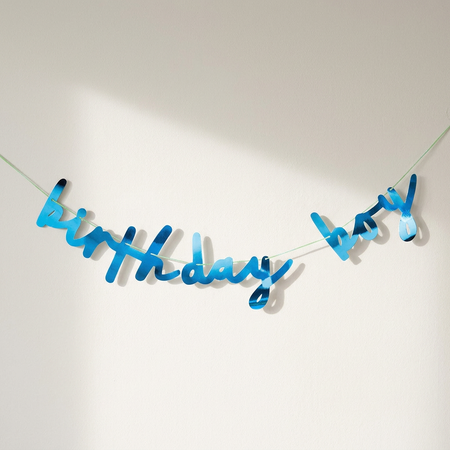 Metallic blue birthday boy banner against an off-white wall with soft light and shade, in square format