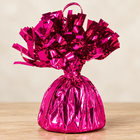 Metallic pink balloon weight close up on a wooden table with a neutral background, in square format