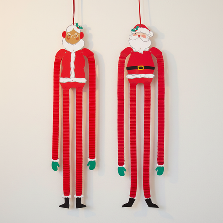 Mrs Claus and Santa hanging paper decorations against a warm off-white wall