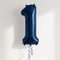 Navy blue number 1 balloon floating with blue curling ribbon against a softly lit white wall, in square format