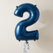Navy number 2 balloon floating with navy curling ribbon against a neutral wall, square close-up