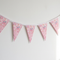One length of pink floral fabric bunting against a white wall with soft light and shade, in square format