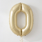 Pale gold number 0 balloon with gold curling ribbon against a softly lit neutral wall