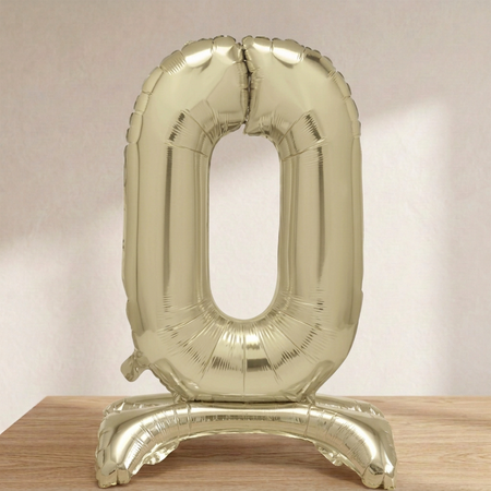 Pale gold number 0 standing balloon on a wooden tabletop with a softly lit neutral background