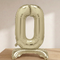Pale gold number 0 standing balloon on a wooden tabletop with a softly lit neutral background