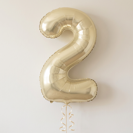 Pale gold number 2 balloon floating with matching curling ribbon against a neutral background with soft light and shade