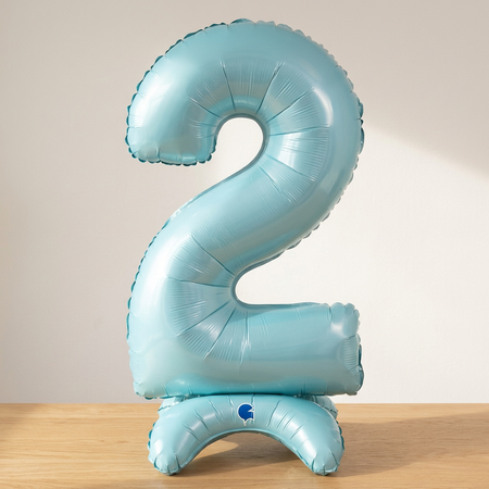 Pastel blue number 2 standing balloon on a wooden table with a softly lit neutral background, square close-up