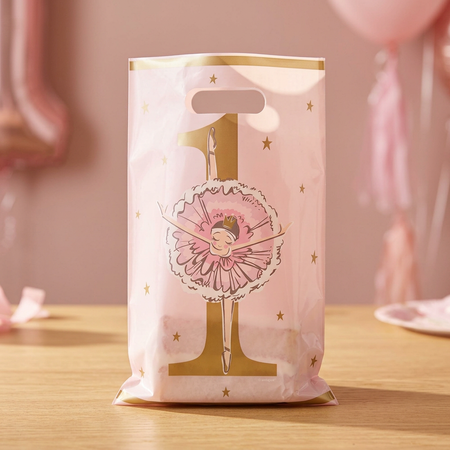 Pink ballerina plastic party bag standing on a wooden table, styled with wrapped birthday cake inside and a soft pink birthday background