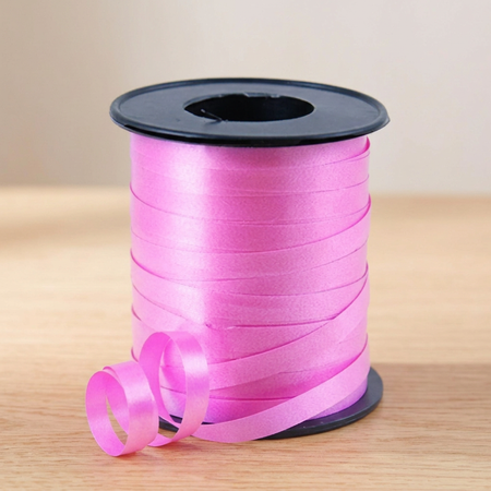 Pink curling ribbon reel on the matching wooden tabletop with a neutral background and soft lighting, in square format